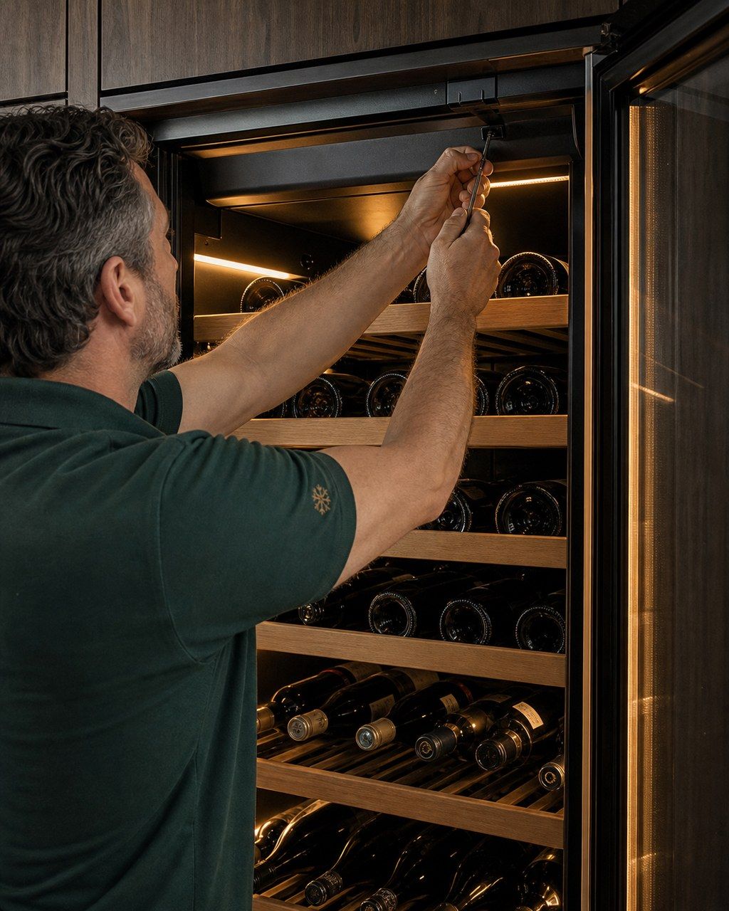 A technician’s hands servicing the interior of a built-in Sub-Zero wine column, checking a small temperature sensor near the top zone with bottles racked below